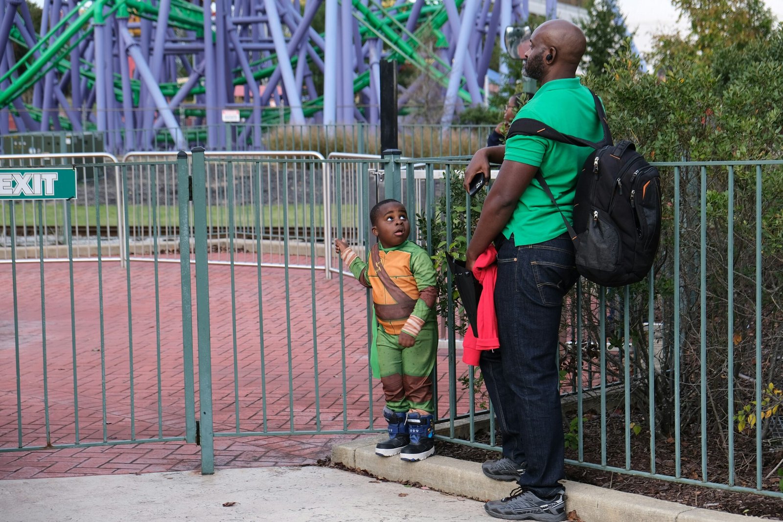 a person and a boy standing by a fence and a roller coaster