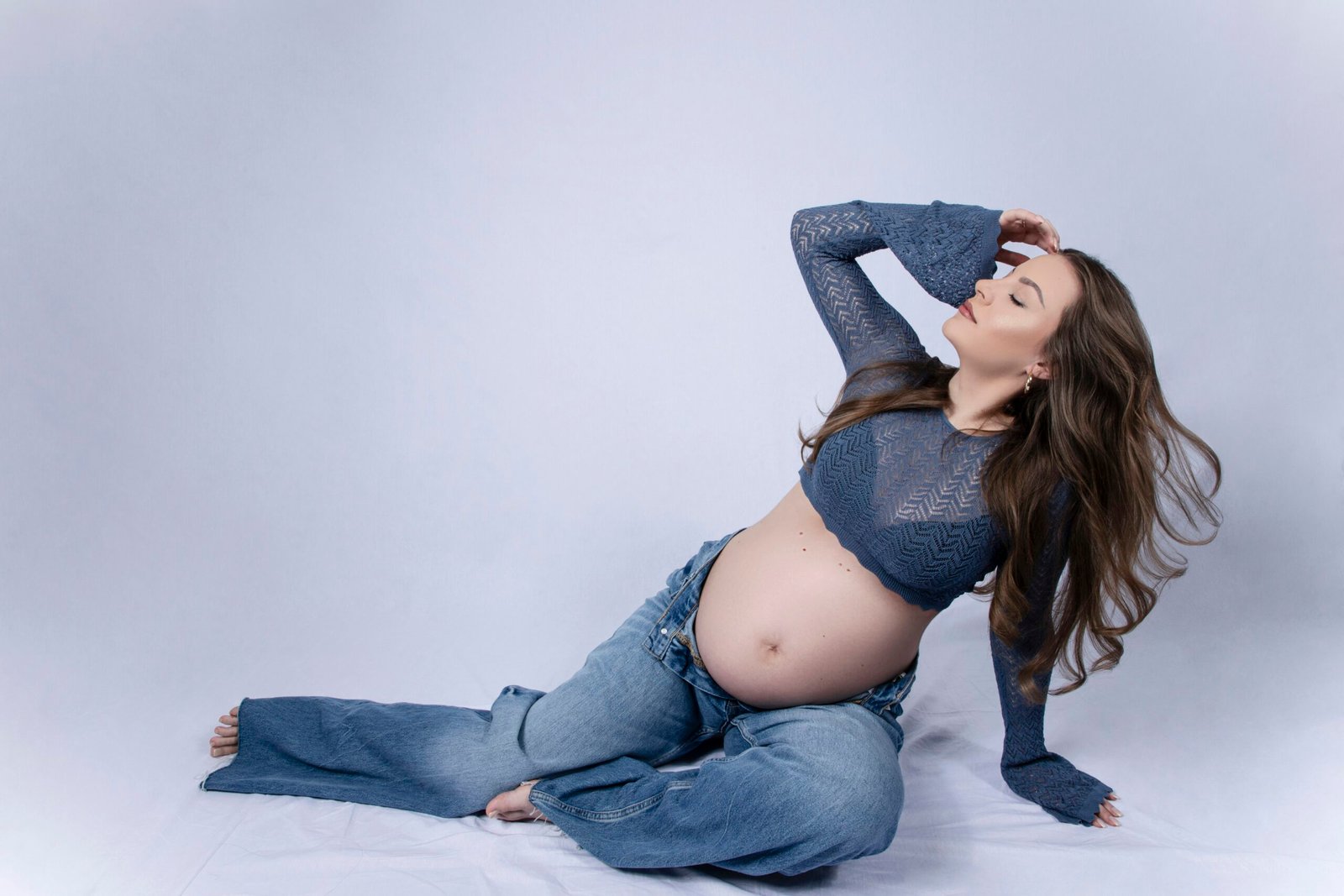 Pregnant woman in jeans and blue top poses gracefully poses gracefully posing