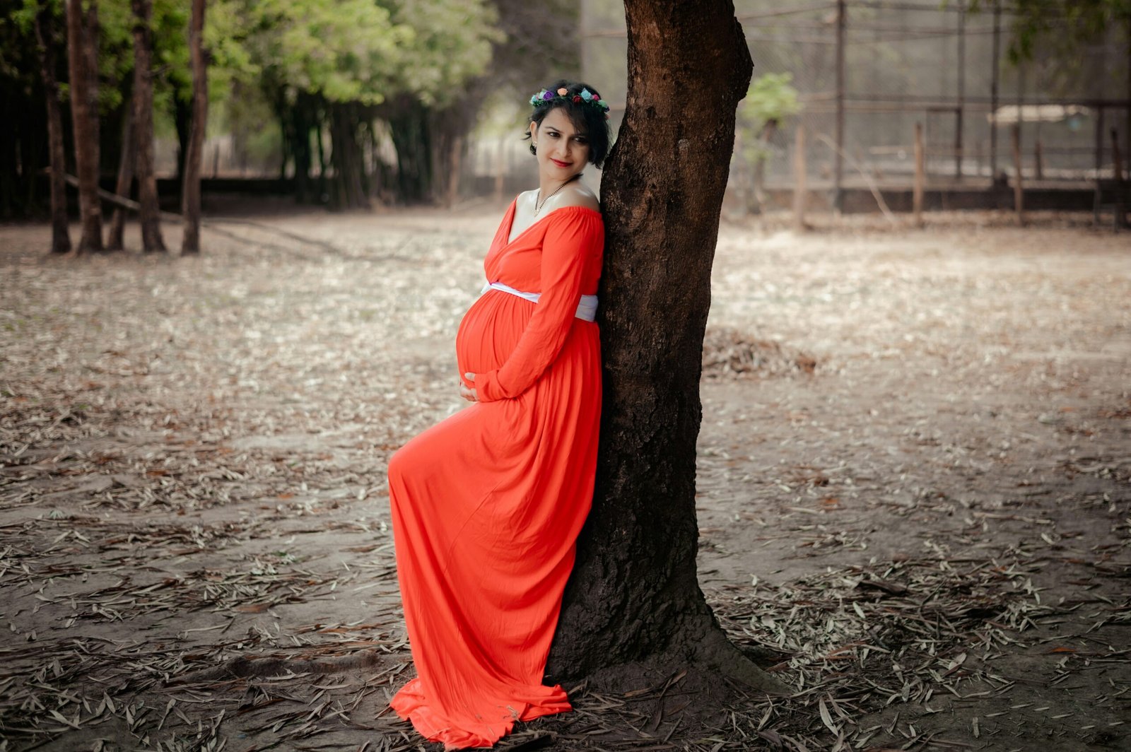 a woman in an orange dress leaning against a tree