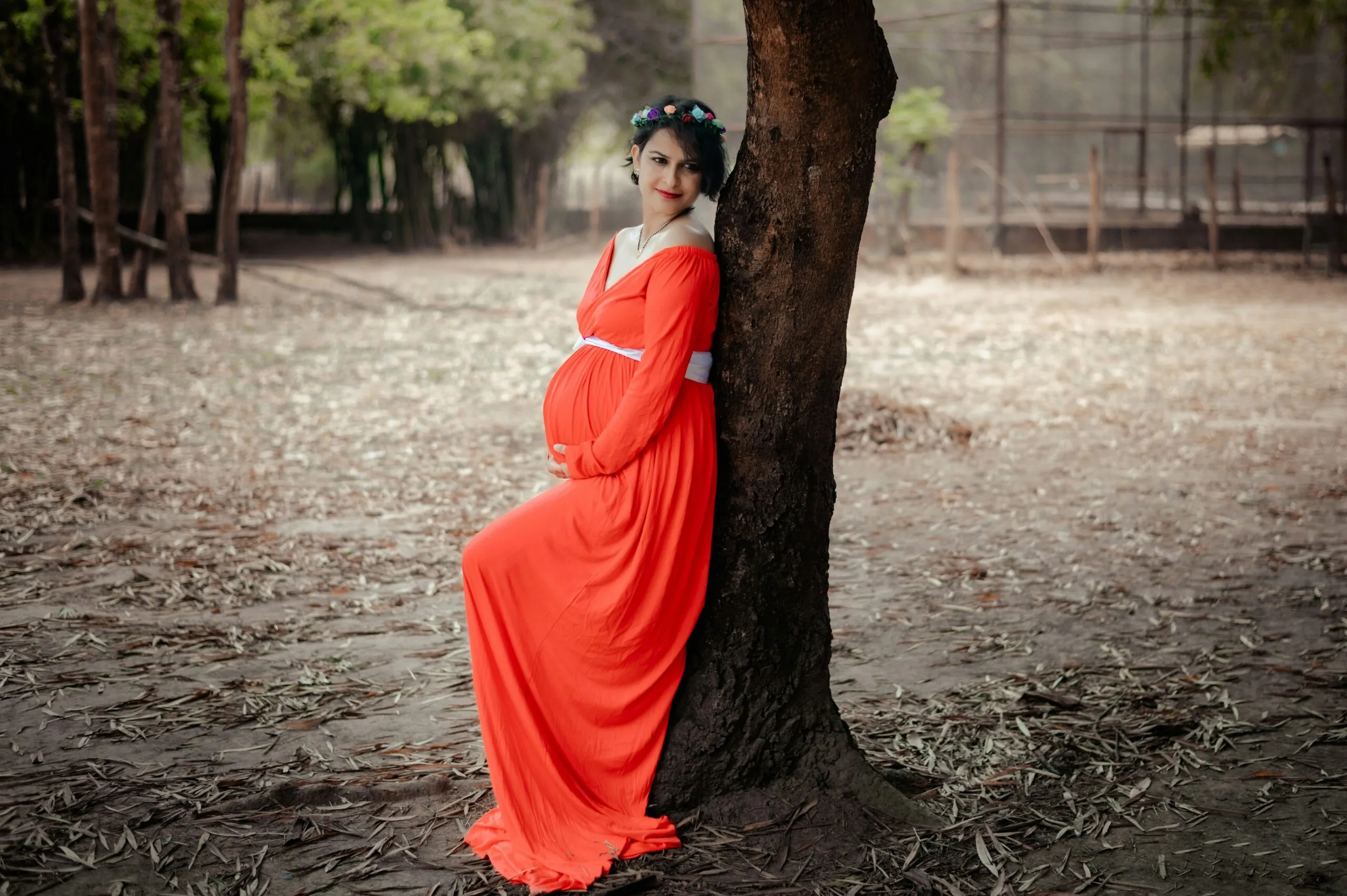a woman in an orange dress leaning against a tree