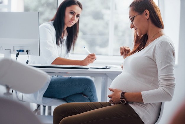 Active conversation. Pregnant woman have consultation with obstetrician indoors.