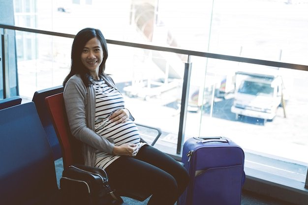 Asian pregnant woman sitting beside a suitcase