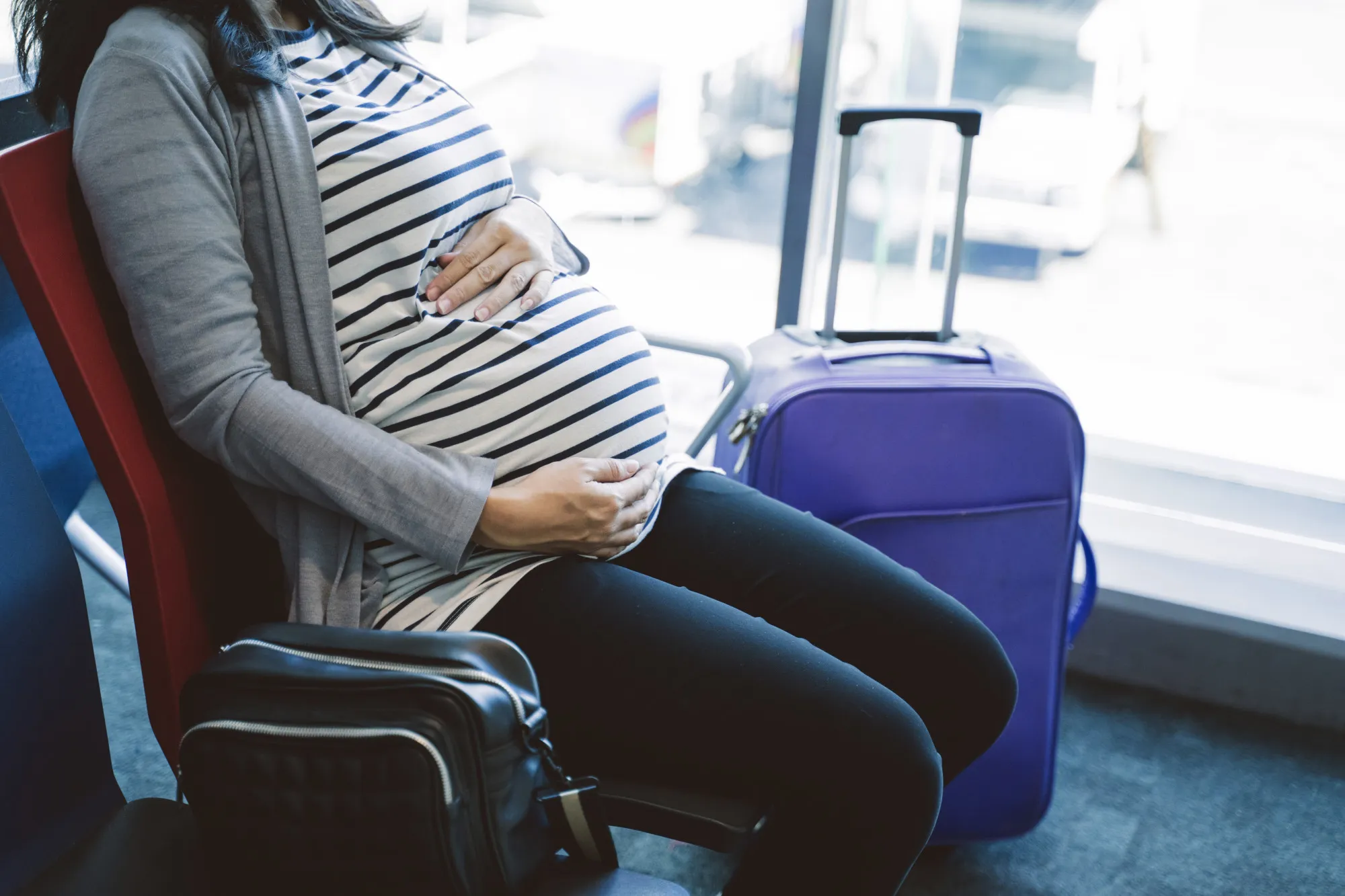 Asian pregnant woman sitting beside a suitcase