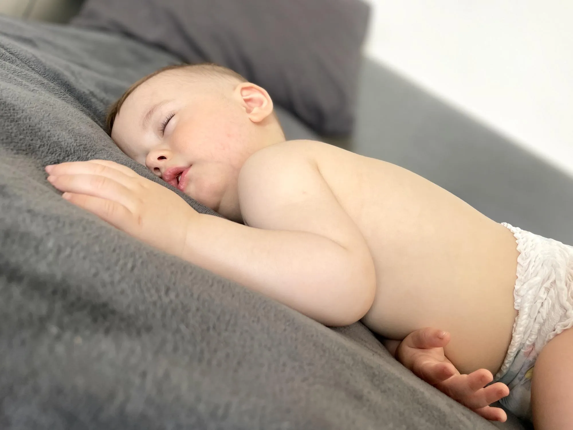 A baby boy sleeps soundly on his stomach during the day on a gray blanket