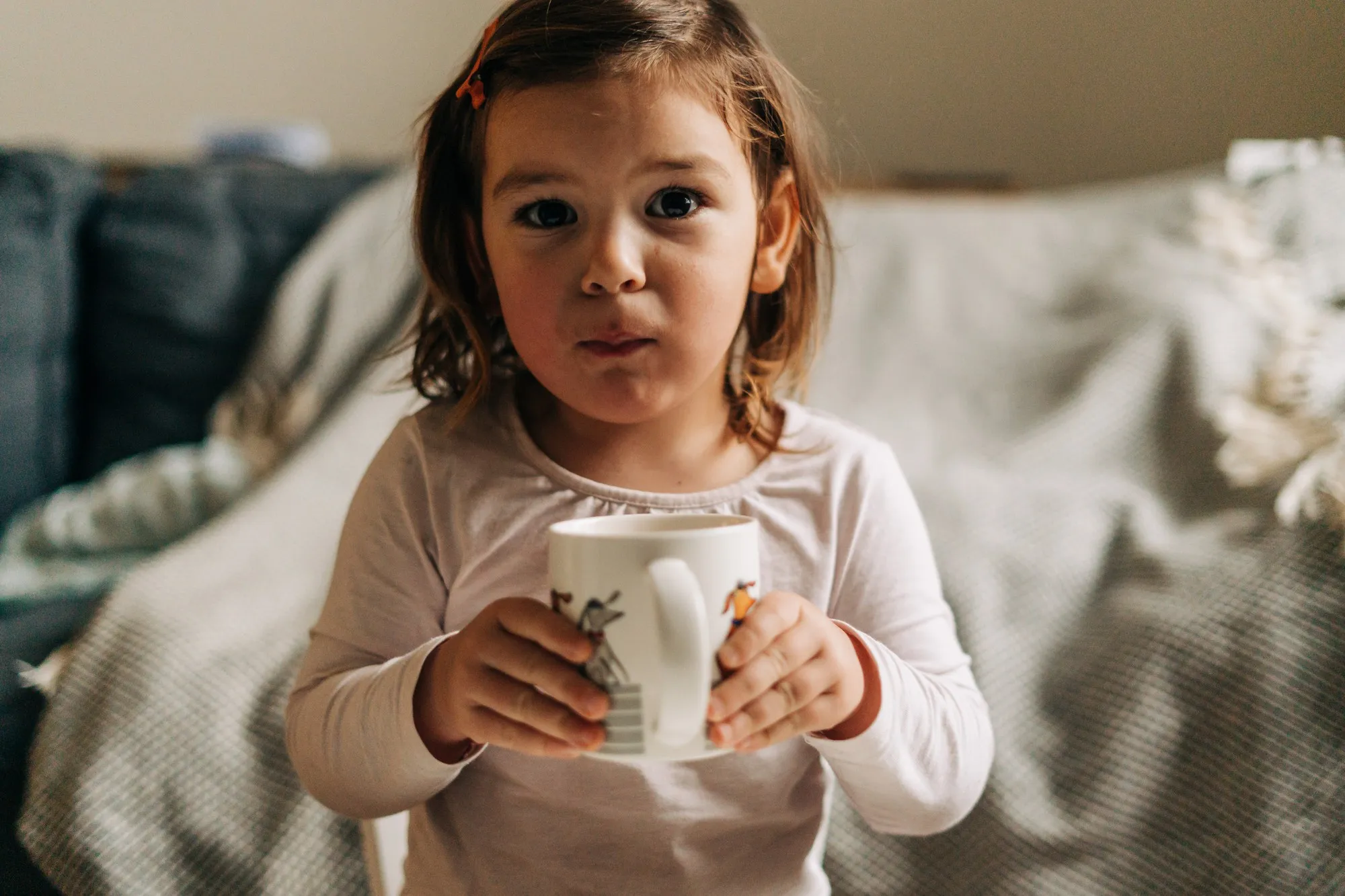 Caucasian toddler girl drinking cocoa from mug at home. Christmas bokeh lights