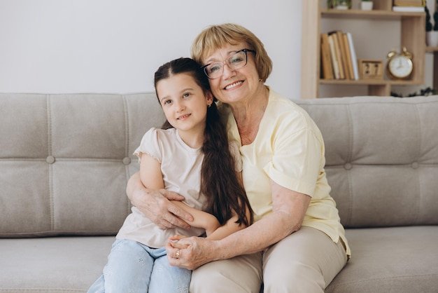 Cheerful cute granddaughter kid and happy grandma hugging with love tenderness affection Grandmother embracing grandchild enjoying family relationship