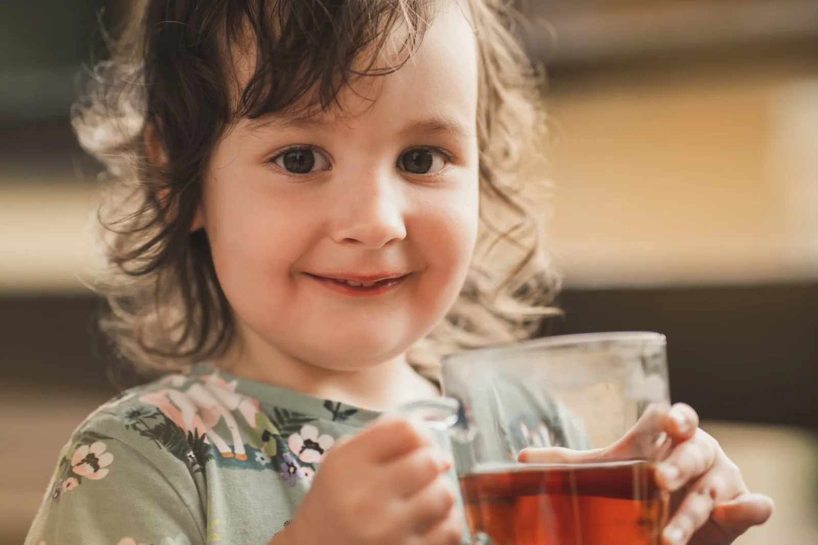 The child drinks tea closeup of the childs face a small and sweet girl looks into the frame and smil...