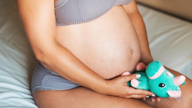 Close-up of the belly of a pregnant woman with a soft toy. The concept of pregnancy, parenthood, preparation and waiting. pregnant belly, natural skin. stretching marks on abdominal skin