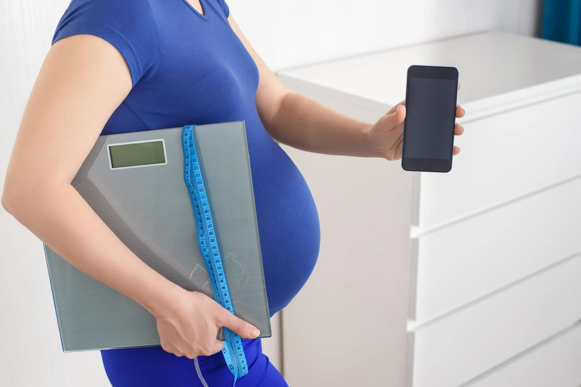 closeup pregnant woman holding scales tape measure and smartphone