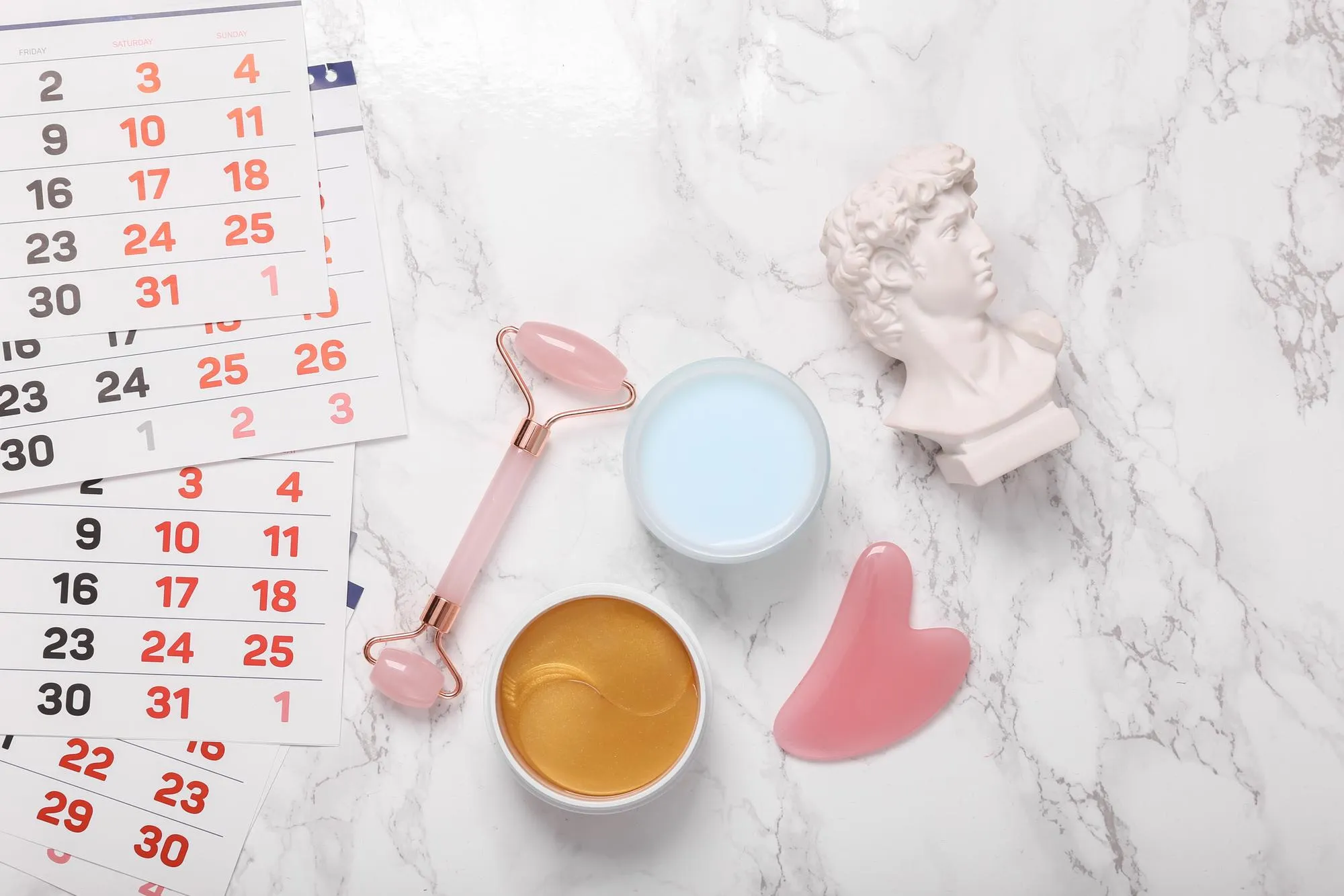 Cosmetic products for facial skin care and David bust calendar on a marble background Flat lay