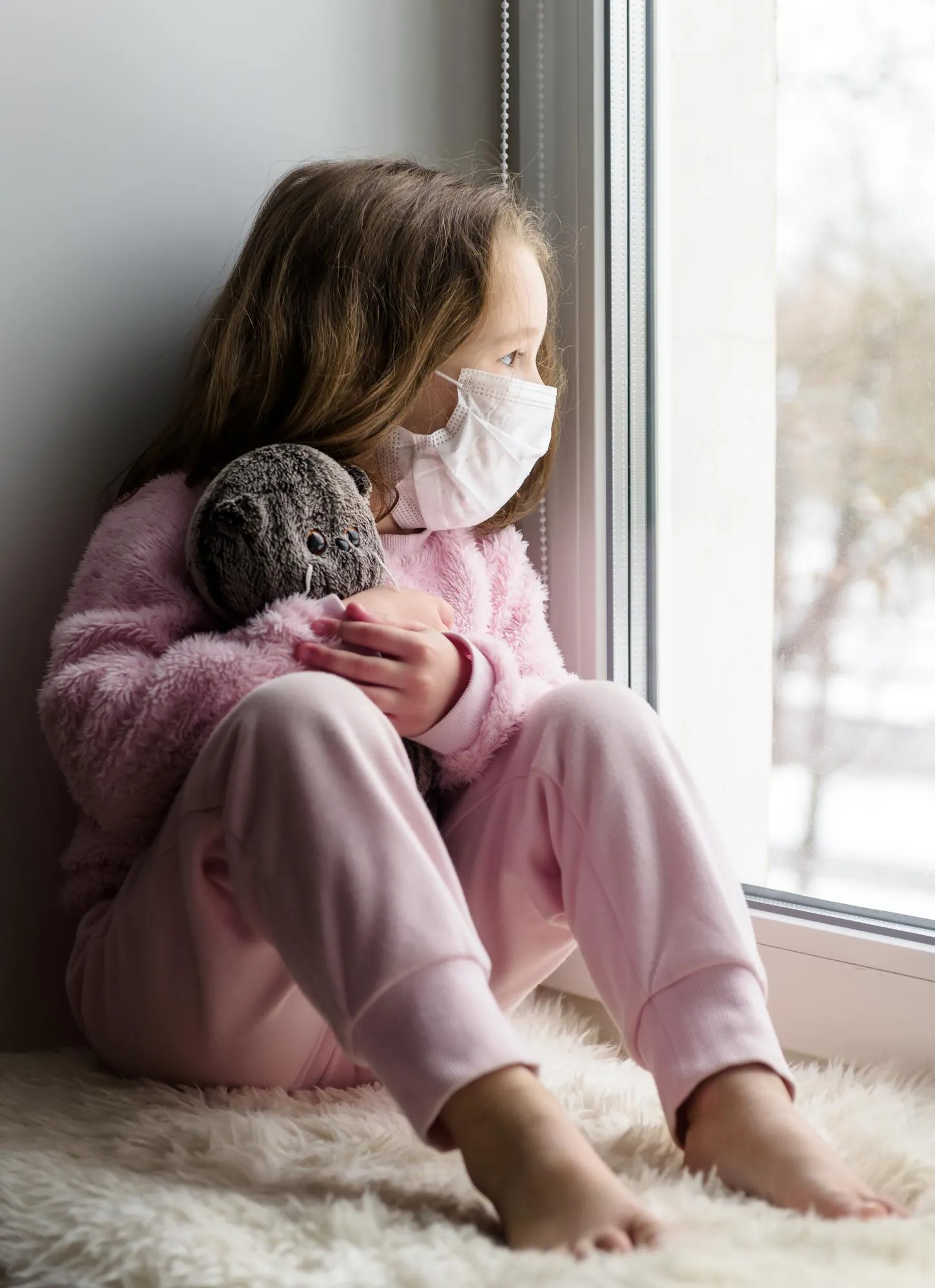 COVID19 coronavirus concept sad kid in medical mask looks out window