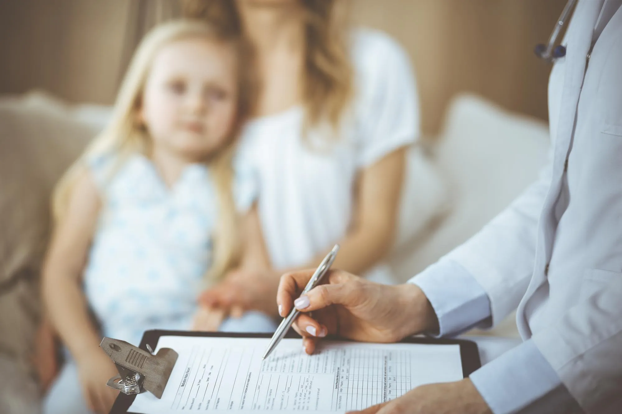 Doctor and patient. Pediatrician using clipboard while examining little girl with her mother at home. Sick and unhappy child at medical exam. Medicine concept.