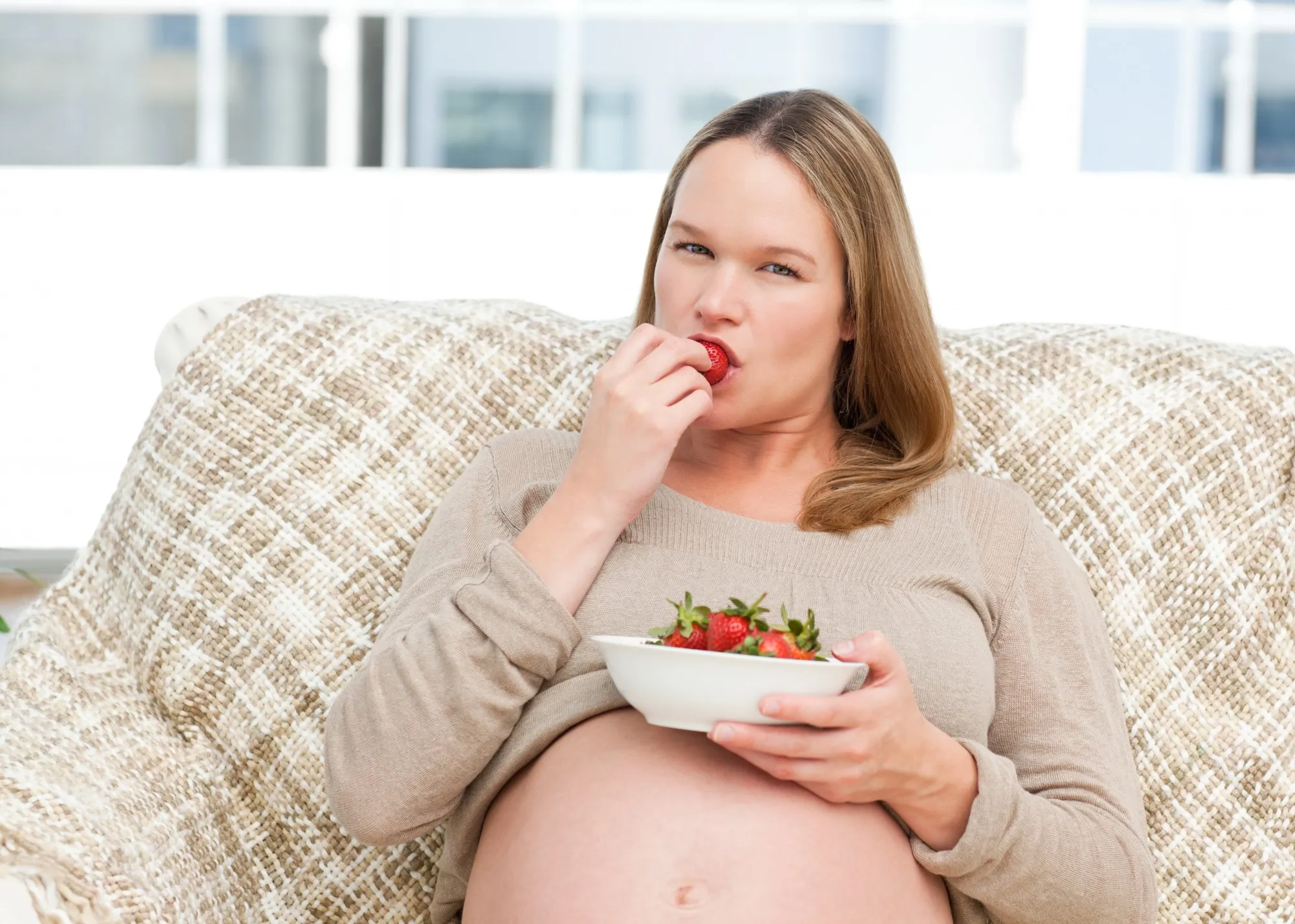 Funny future mom eating strawberries resting on the sofa
