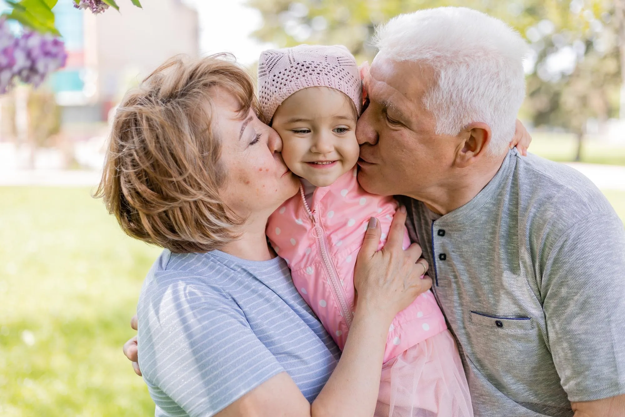 grandma and grandpa hug and hold a charming little granddaughter in their arms family walk