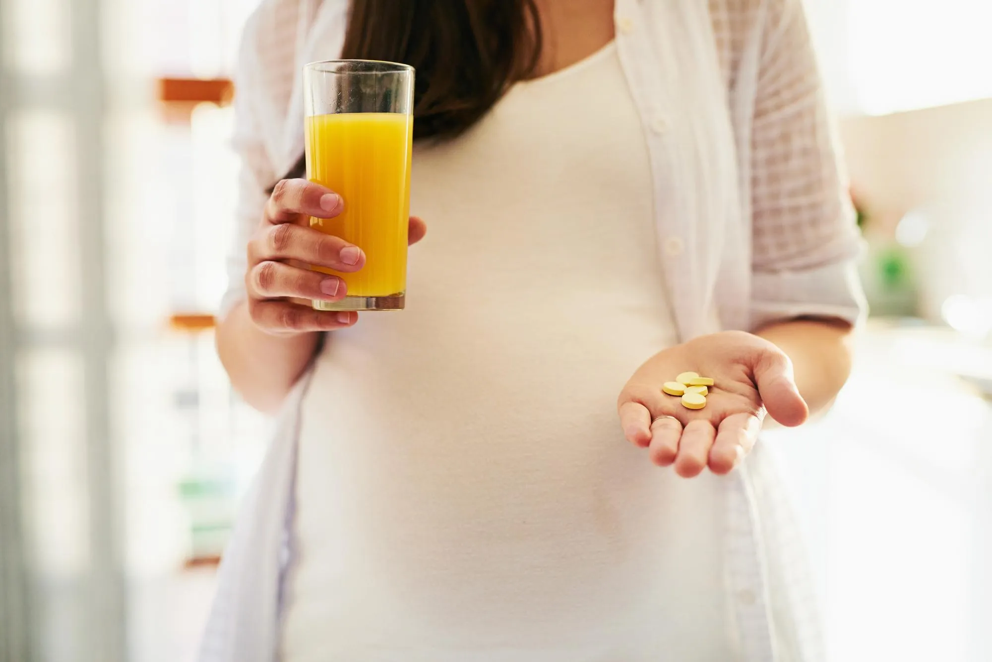 Hands pregnant woman and pills with juice for health supplements and start morning in home Person mother and orange drink for nutrition diet and pharma drugs for wellness benefits and change