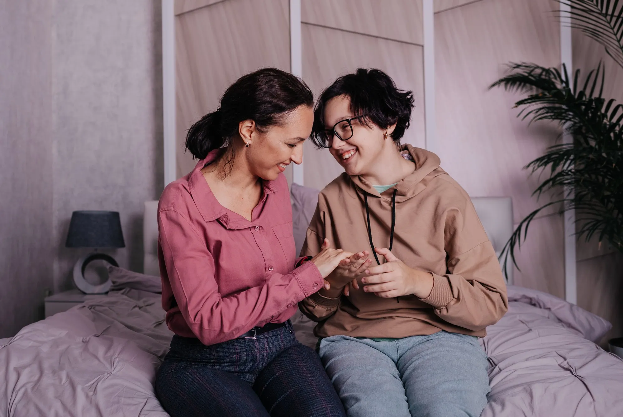 Happy brunette mom with a teenage daughter sitting on the bed in the room and chatting