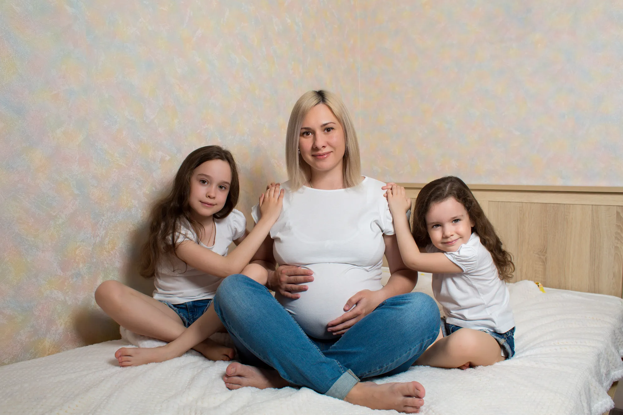 Happy pregnant woman with her daughters sitting on bed at home. happy family in isolation. Kids love for their mother