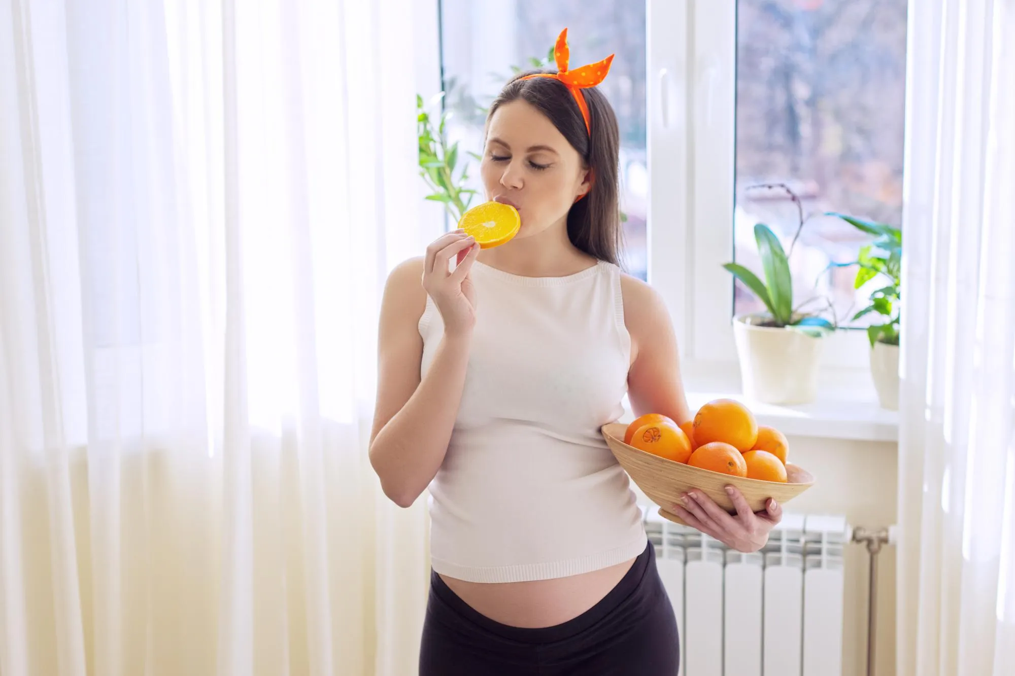 Healthy vitamin food, Beautiful happy pregnant young woman with oranges at home near the window. Pregnancy, vitamins, motherhood concept