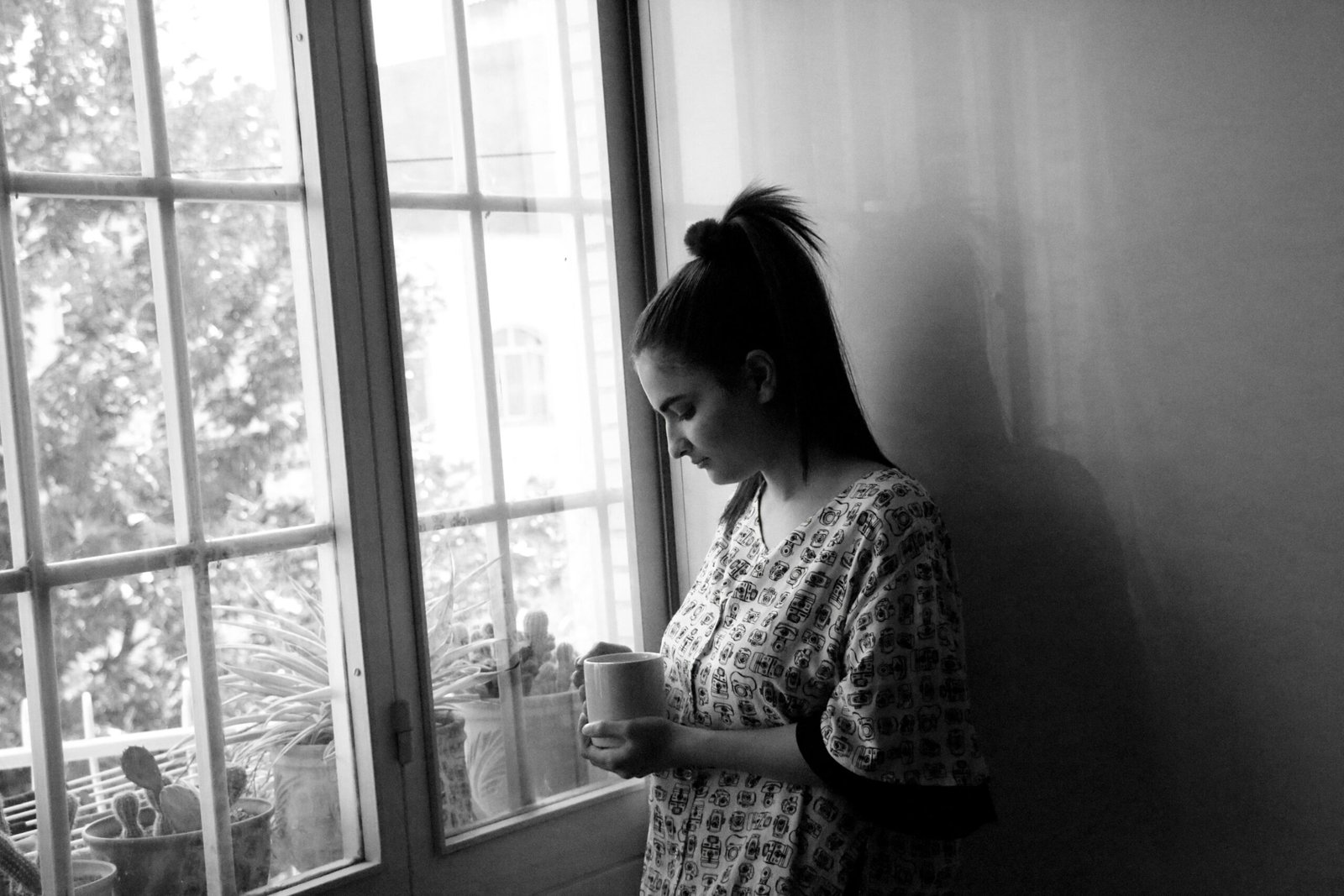 A woman standing in front of a window holding a cup