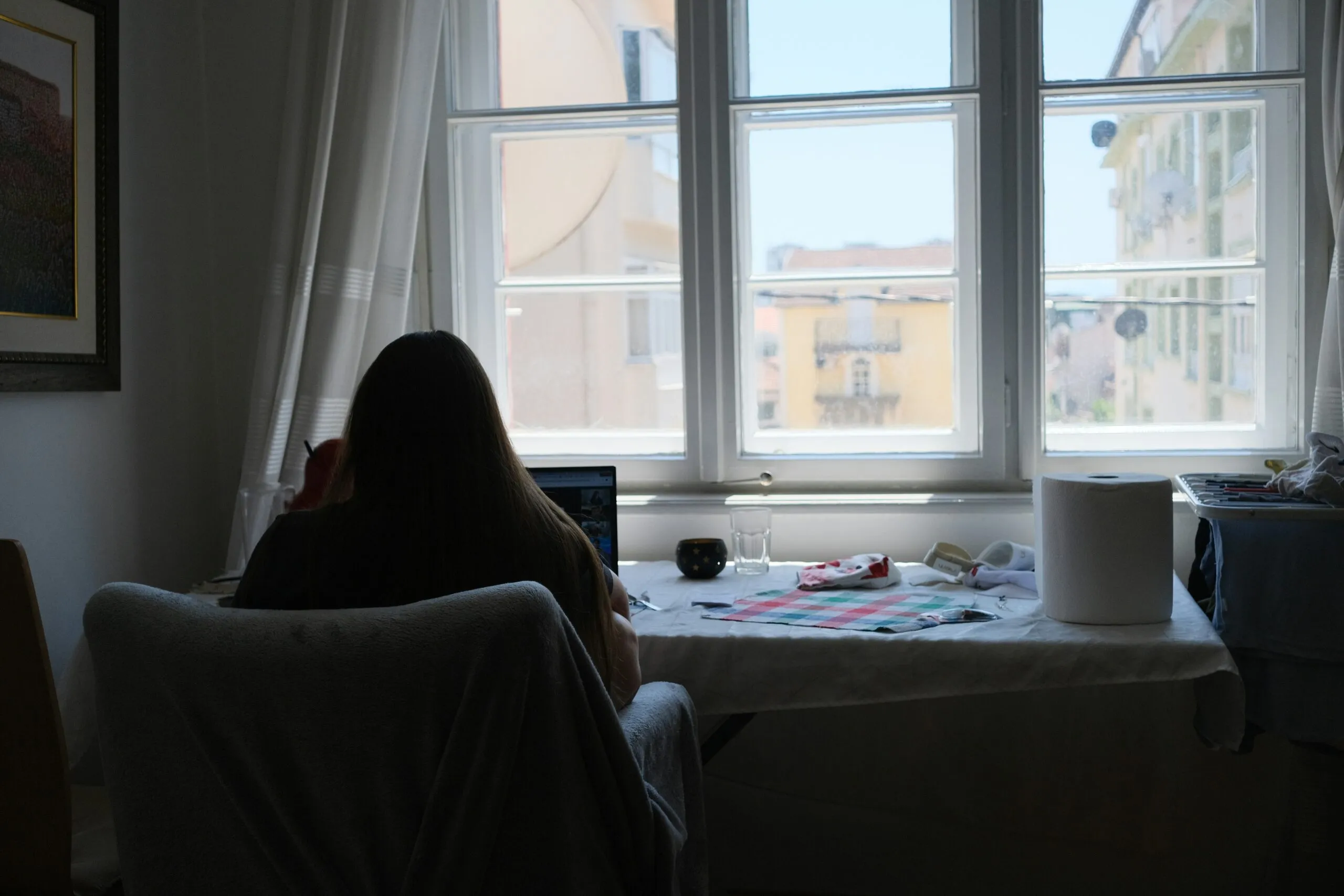 Person works near a bright window in a room.