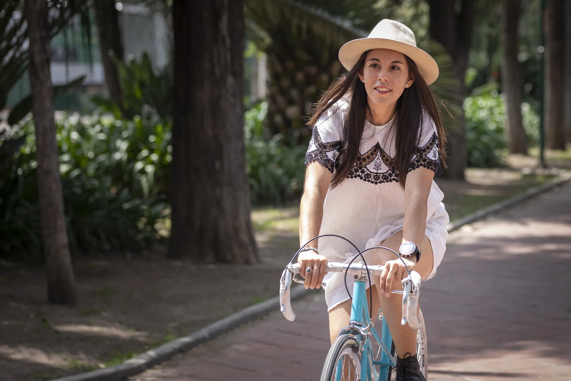 Latin woman in white dress and hat walking with bicycle in the park