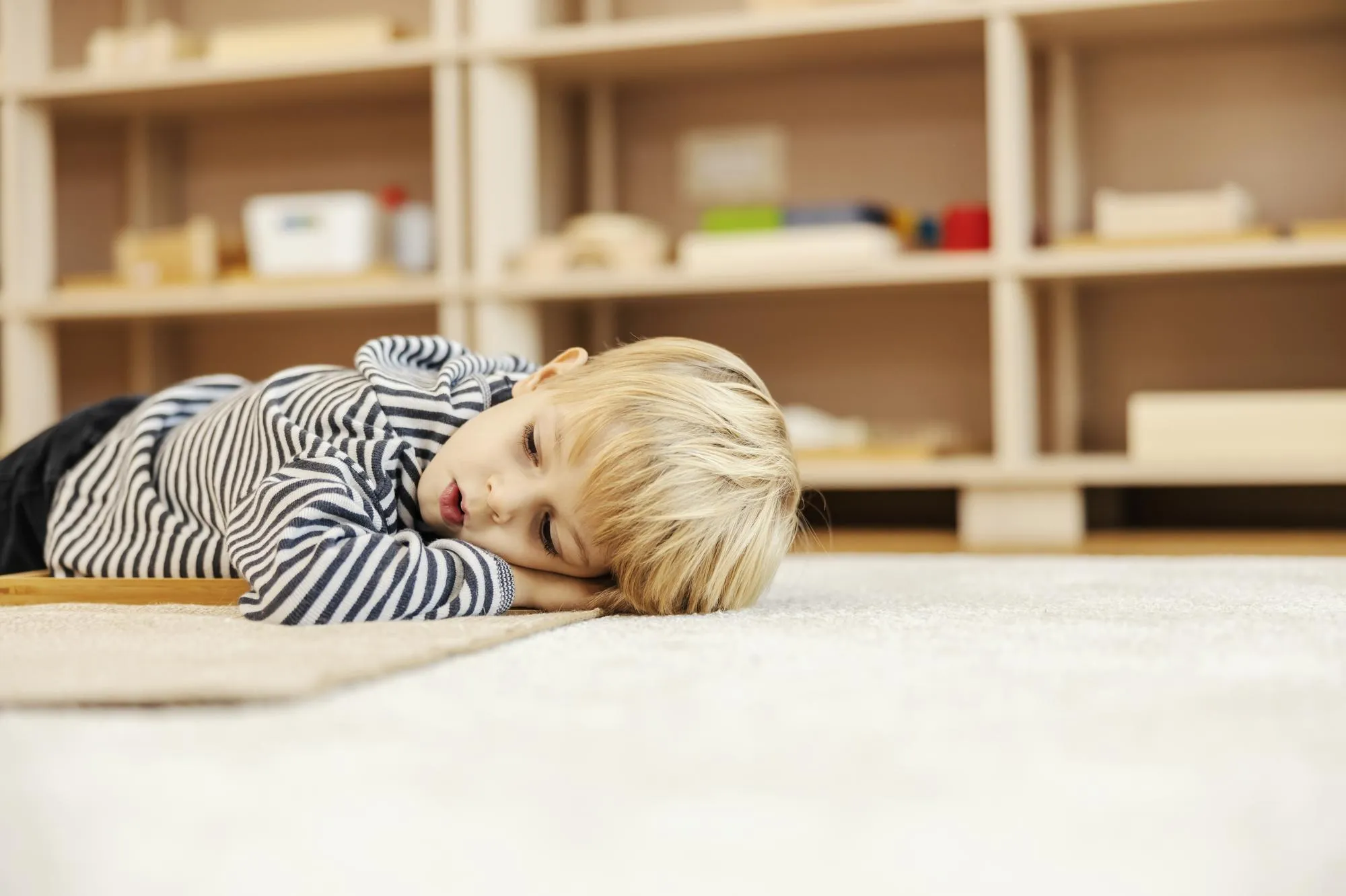 A little boy is taking a break and lying down on the floor in kindergarten