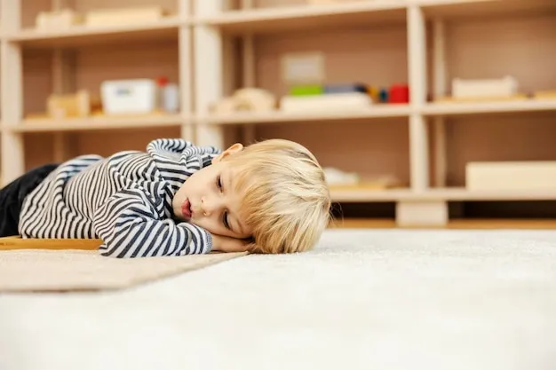 A little boy is taking a break and lying down on the floor in kindergarten