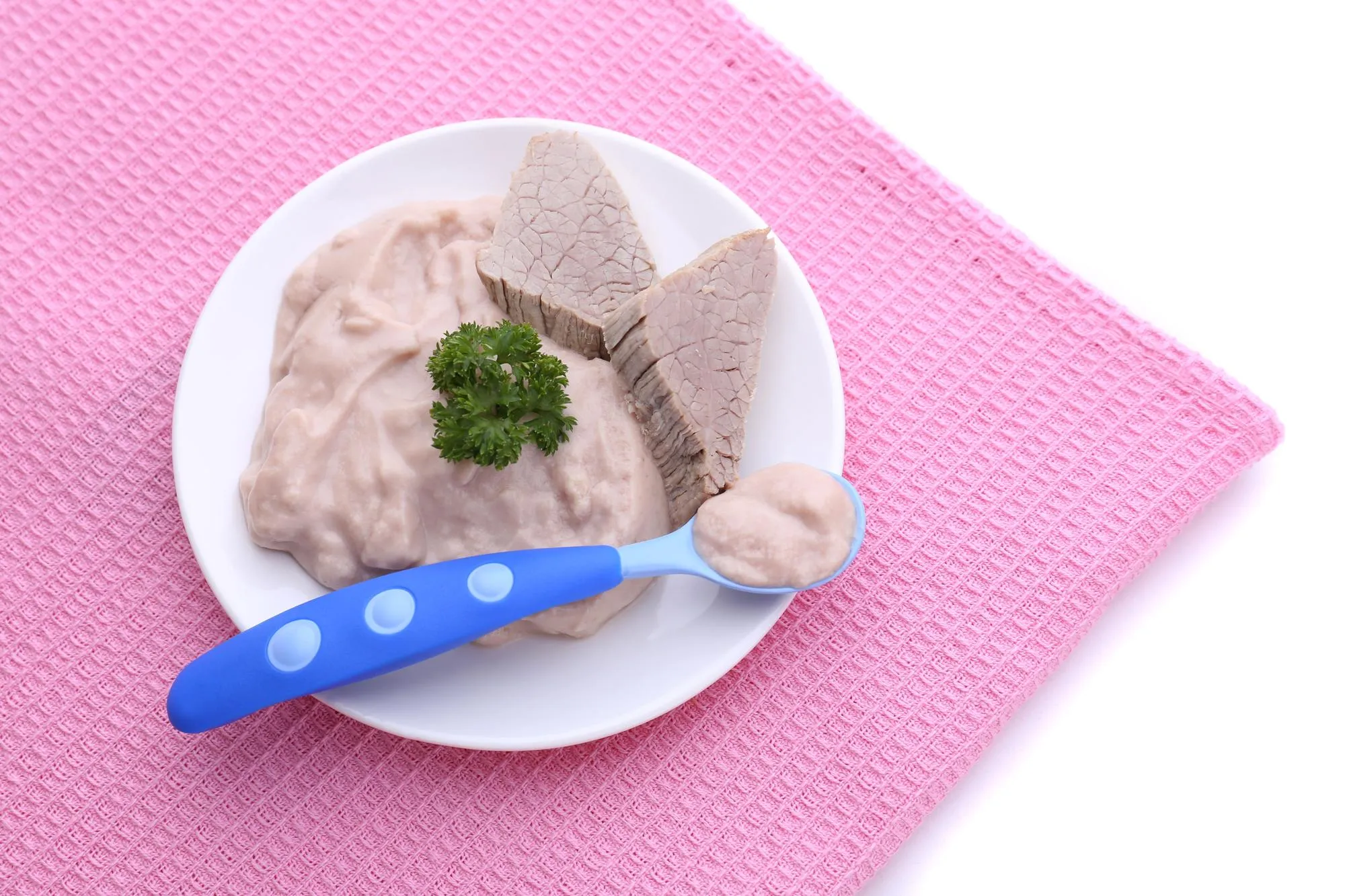 Meat paste for infant feeding on plate on color napkin isolated on white