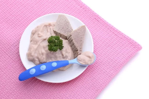 Meat paste for infant feeding on plate on color napkin isolated on white