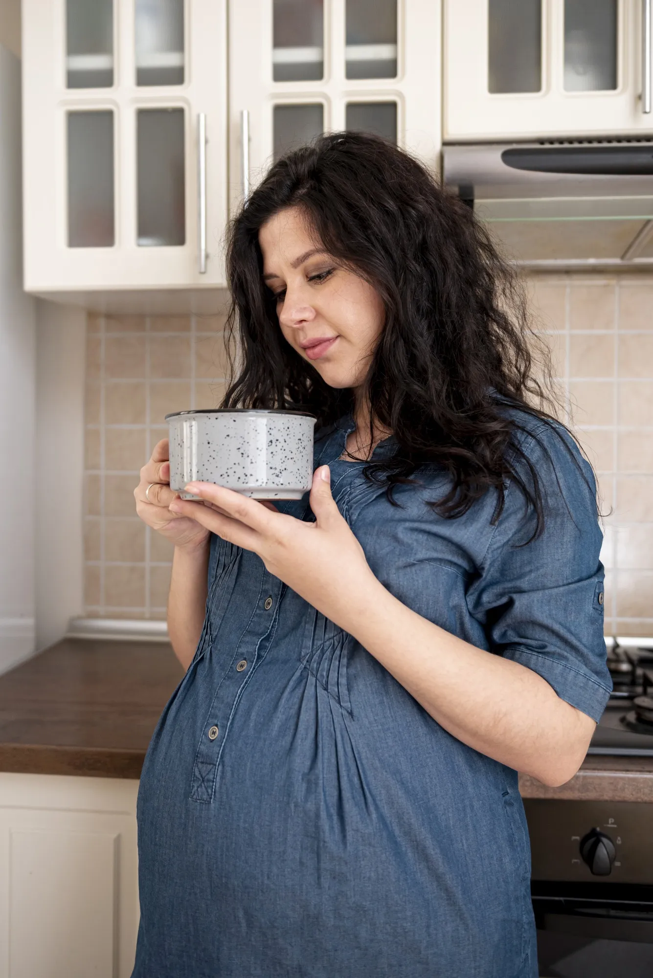 Medium shot pregnant woman with bowl in the kitchen