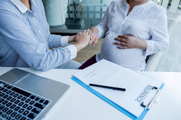 Midsection of insurance agent holding hands with pregnant woman in office