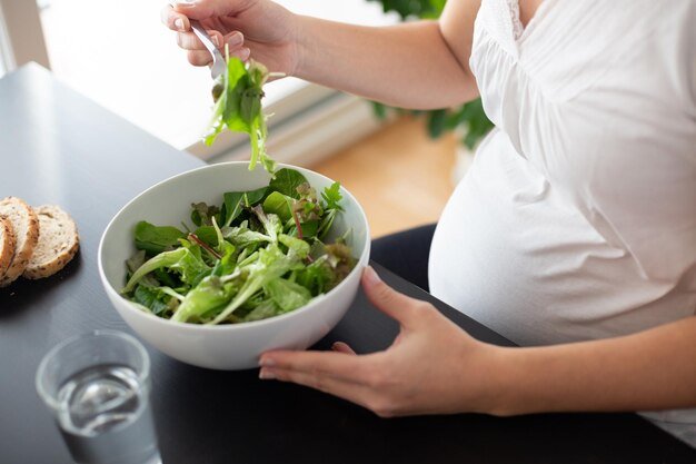 Midsection of pregnant woman eating salad at home