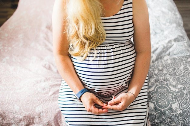 Midsection of pregnant woman sitting on bed