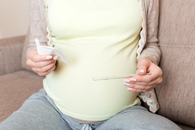 Midsection of pregnant woman taking vitamin pill on sofa at home