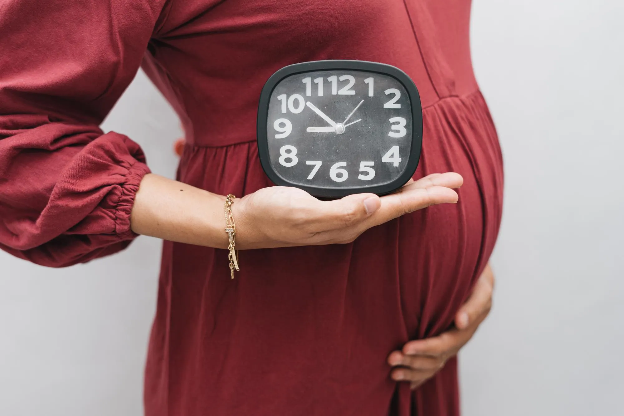 Muslim pregnant woman holding her belly stomach and clock watch