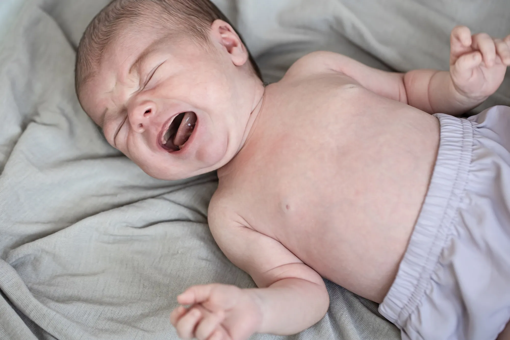 Newborn baby boy crying lying in the crib closeup