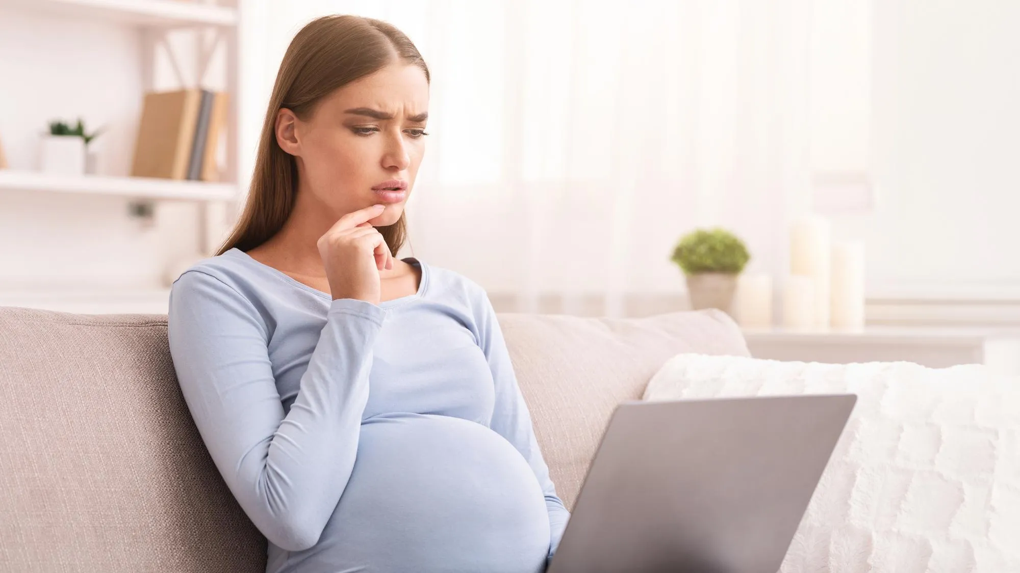 Pensive Pregnant Woman Using Laptop Sitting On Couch At Home