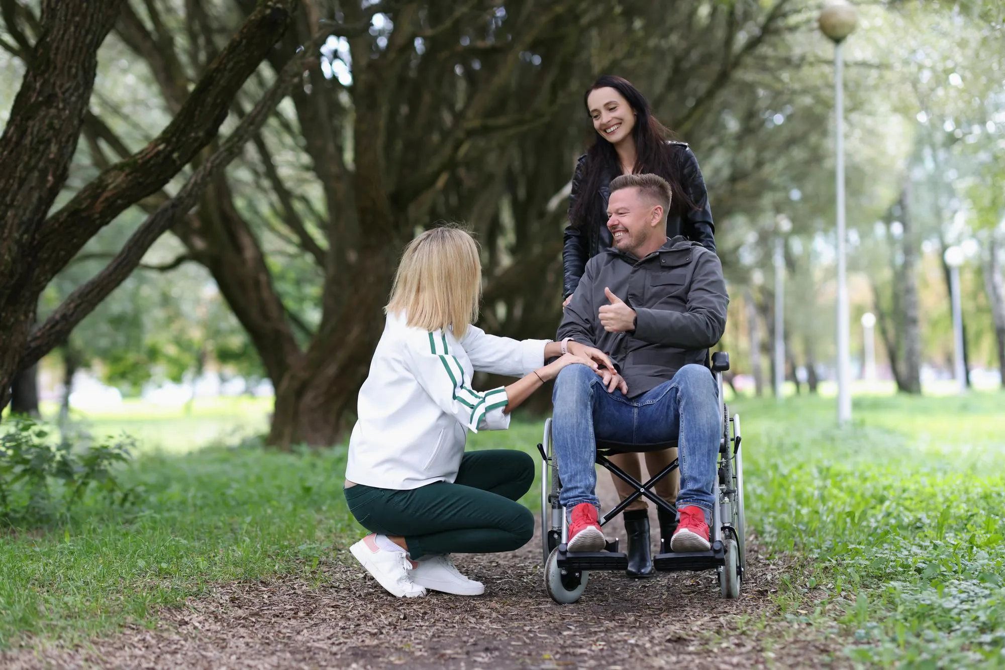 Portrait of women friends walking with disabled man in wheelchair in park disability and