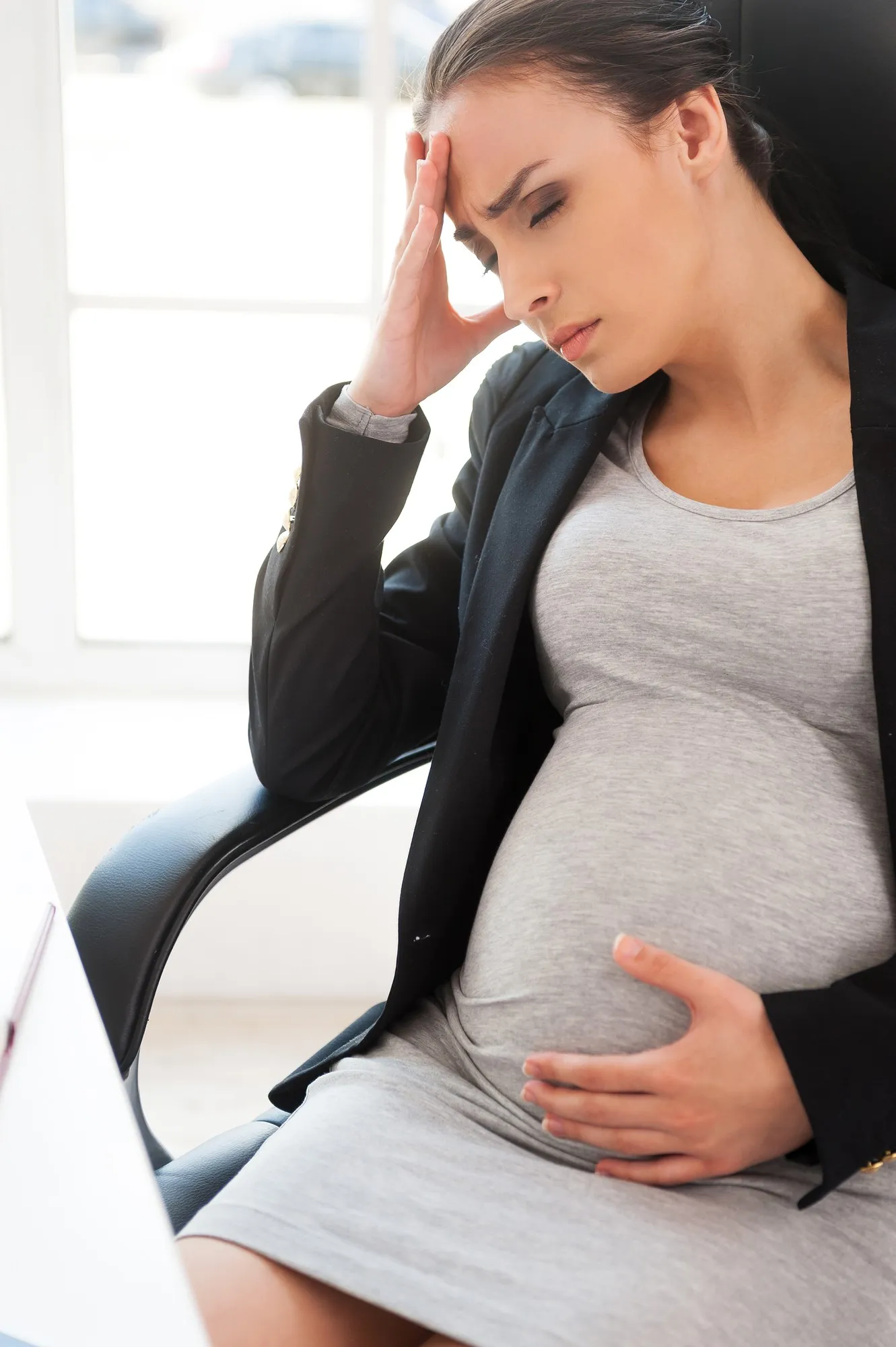 Pregnancy trials. Depressed pregnant businesswoman holding head in hand while sitting at her working place in office