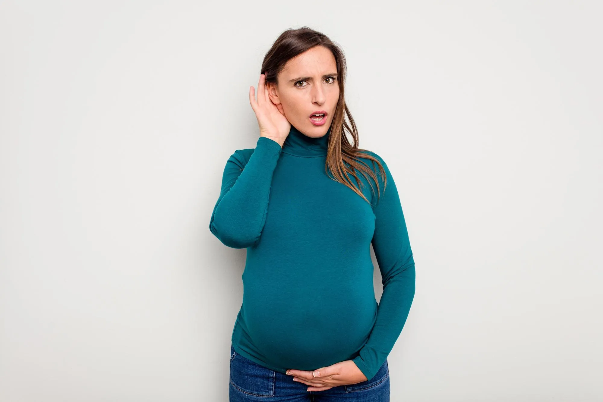 Pregnant caucasian woman isolated on white background trying to listening a gossip
