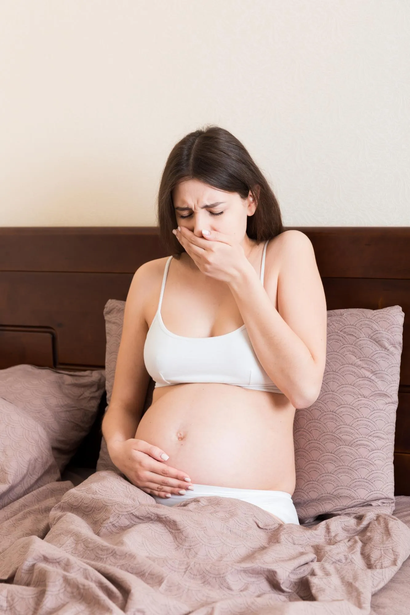 Pregnant suffering with nausea Pregnancy symptoms expectation toxicosis Young vomiting woman sitting on bed parenthood concept