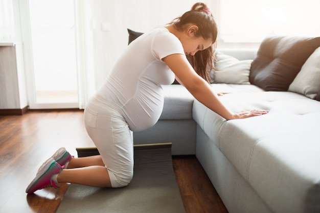 Pregnant woman doing workout at home using a sofa