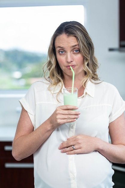 Pregnant woman drinking a smoothie in the kitchen
