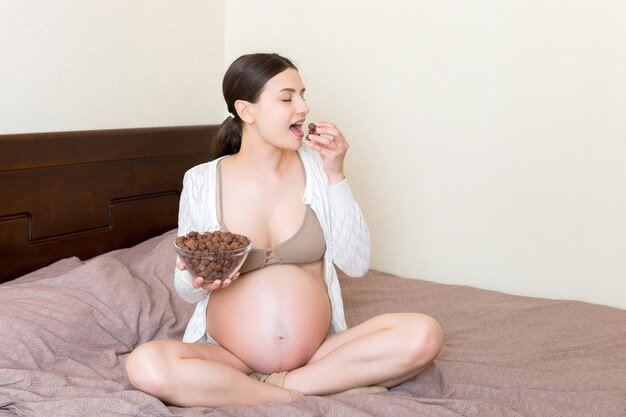 Pregnant woman enjoys eating crunchy chocolate cereal balls from a bowl dieting during pregnancy