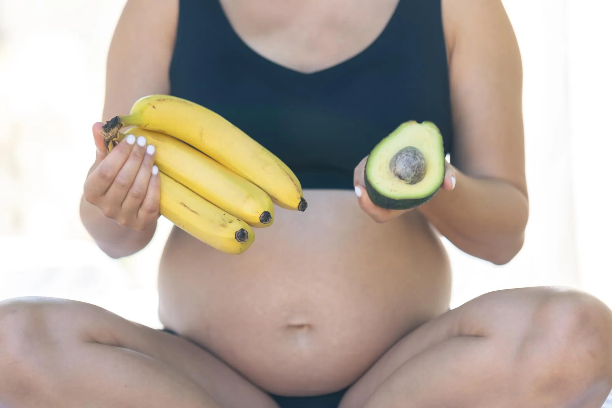Pregnant woman holding avocado and bananas health and maternity concept