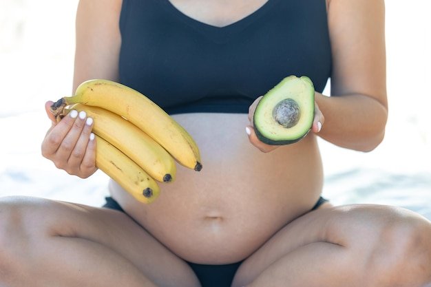 Pregnant woman holding avocado and bananas health and maternity concept
