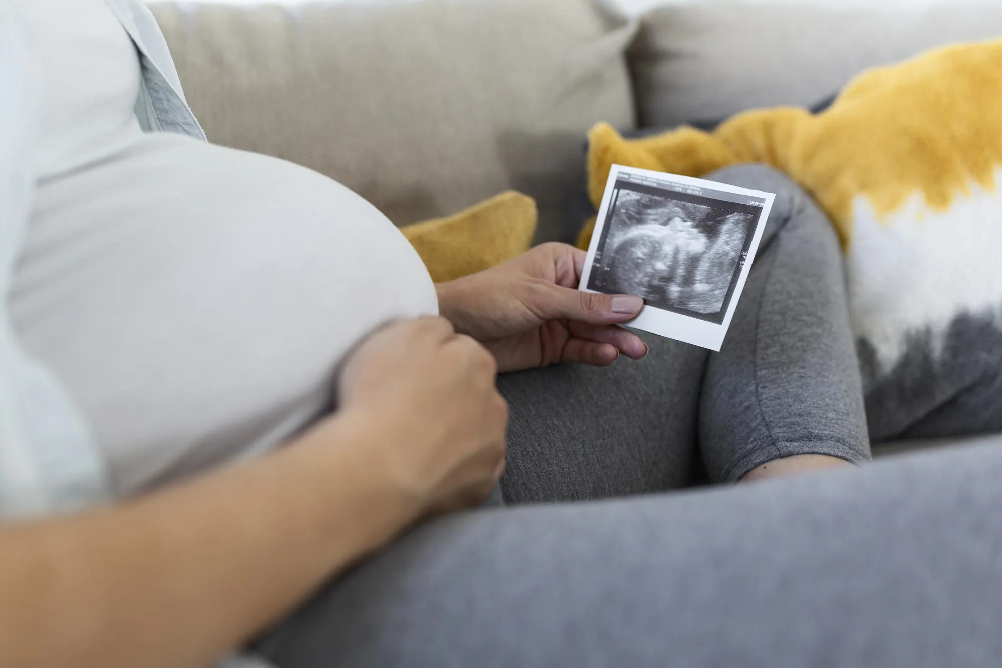Pregnant woman holding ultrasound image. Concept of pregnancy, health care, gynecology, medicine. Young mother waiting of the baby. Close-up, copy space, indoors.