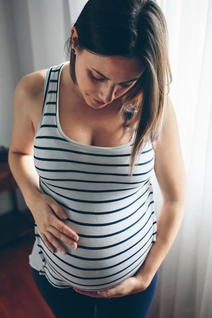 Pregnant woman looking her belly in front of a curtain