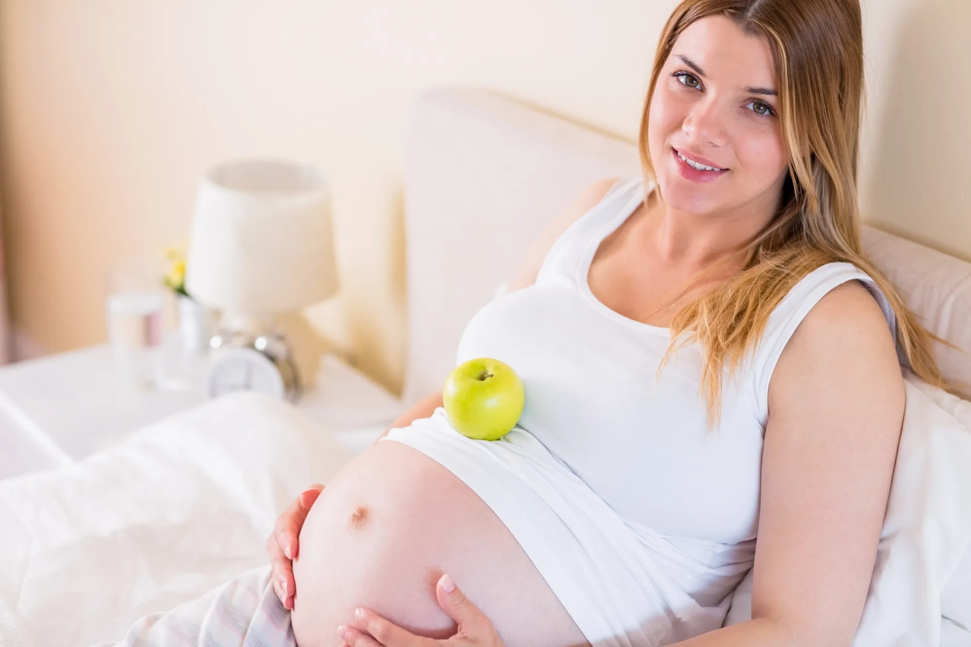 Pregnant woman lying on bed with apple in belly