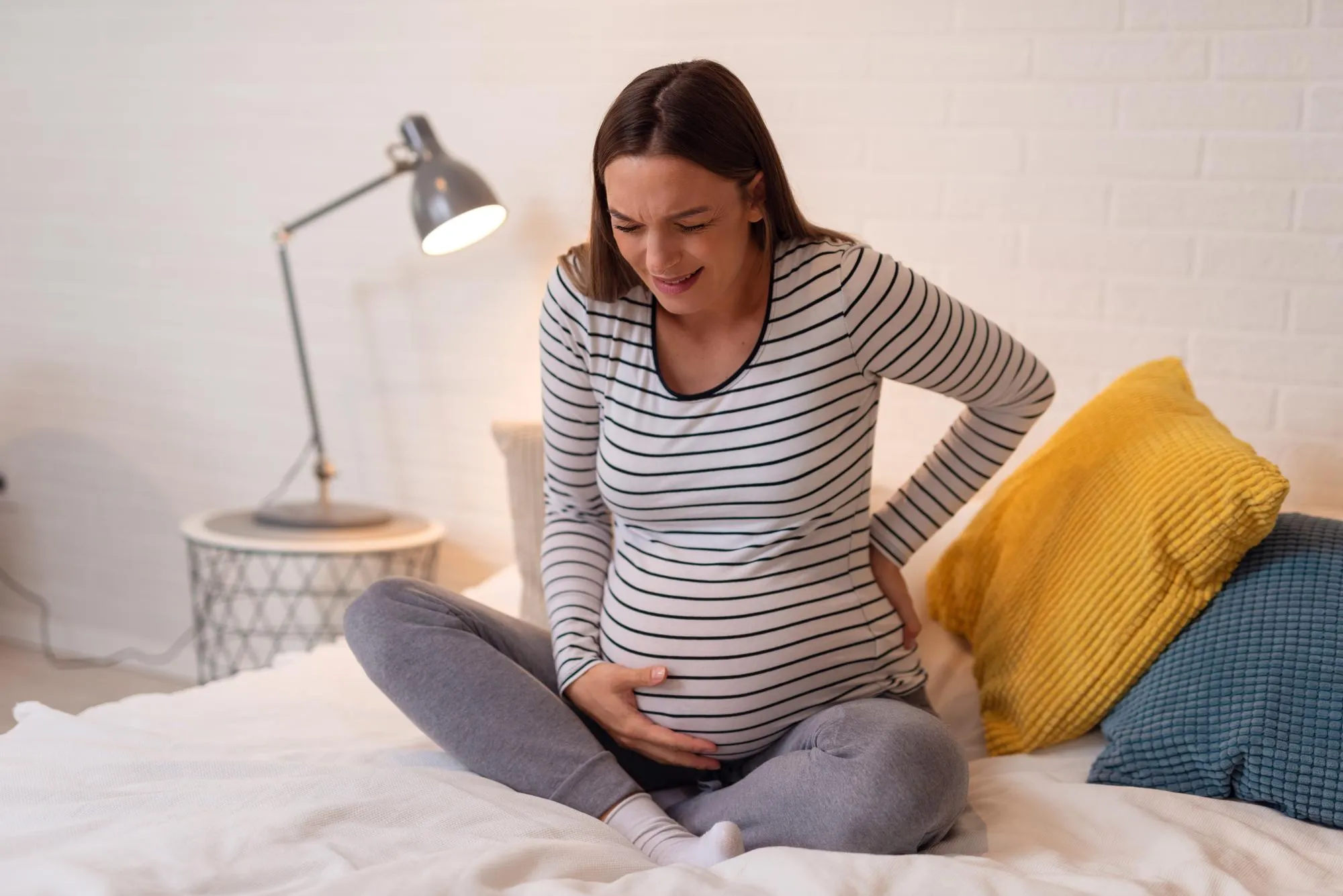 Pregnant woman suffering lower back pain. Woman getting a contraction and backache at home